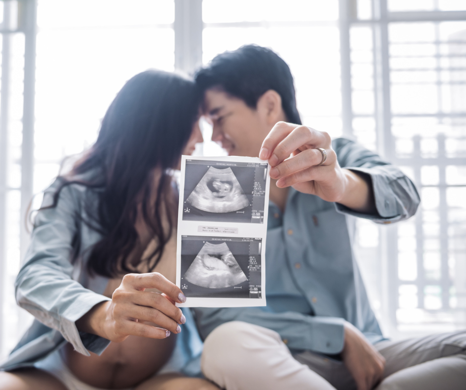 Happy couple hold up 2 ultrasound scan pictures of their unborn baby. 