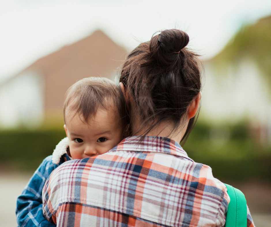 Baby cuddles up to a mum wearing a chequered shirt and mum bun.