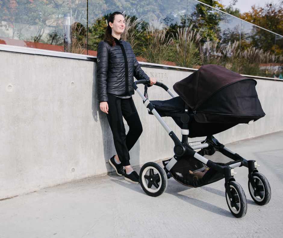 Woman in black jacket stands next to a newborn pram