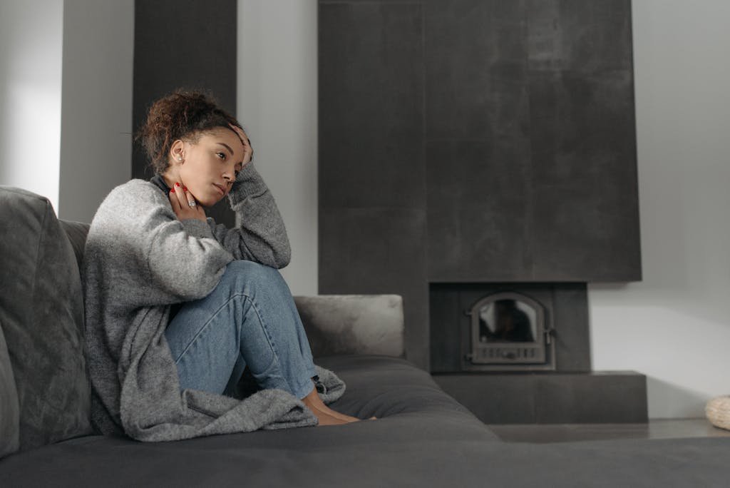 A woman in a cozy living room feeling unwell, sitting on a sofa with a thoughtful expression.