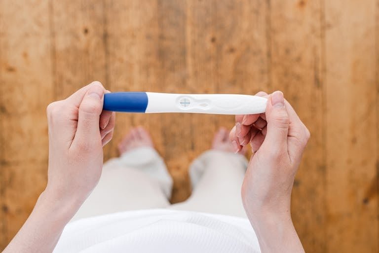 Overhead view of a woman holding a positive pregnancy test indoors.