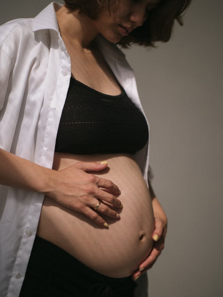Close-up of a pregnant woman gently holding her baby bump during a maternity shoot indoors.