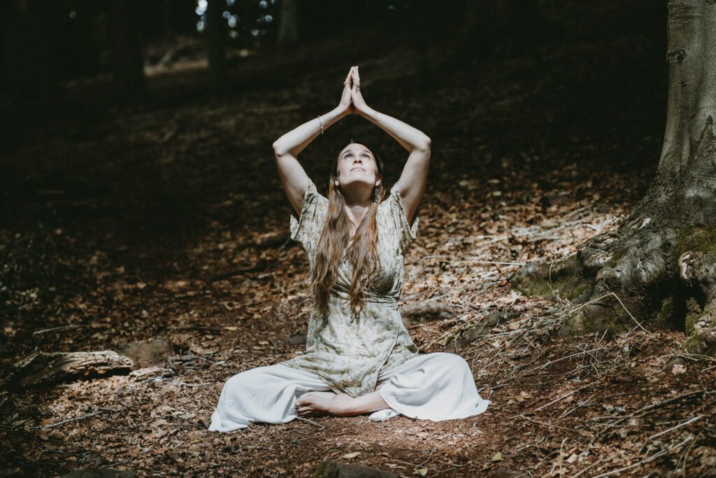 One Positive Birth Story (and how it changed everything) Nicole Harwood, a doula in Bristol, sits amongst the trees whilst in a yoga pose with her hands in the air.