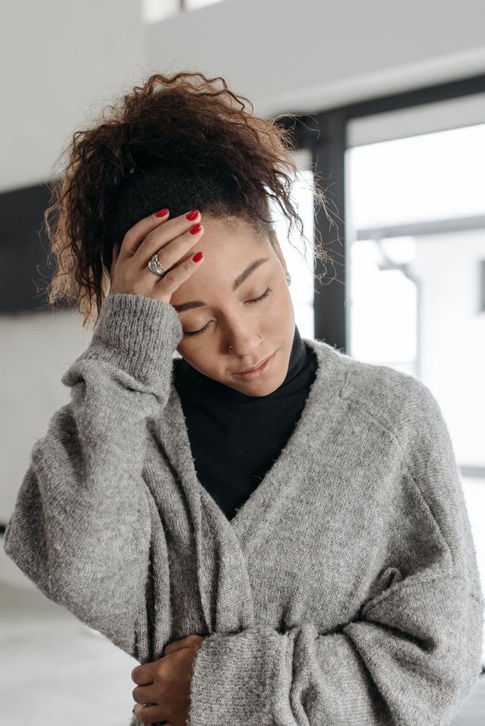 Early Pregnancy Headaches: Causes & Safe Relief 4 A young woman with an early pregnancy headache, wearing a cozy sweater indoors, holds her hand to her head.