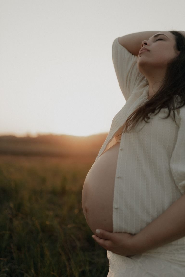Peaceful pregnant woman enjoying sunset in an open field, embracing nature and motherhood.