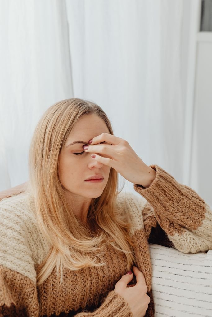 Early Pregnancy Headaches: Causes & Safe Relief 2 Woman suffering from early pregnancy headaches, wearing a cozy sweater in an indoor setting, holds her hand to her head.